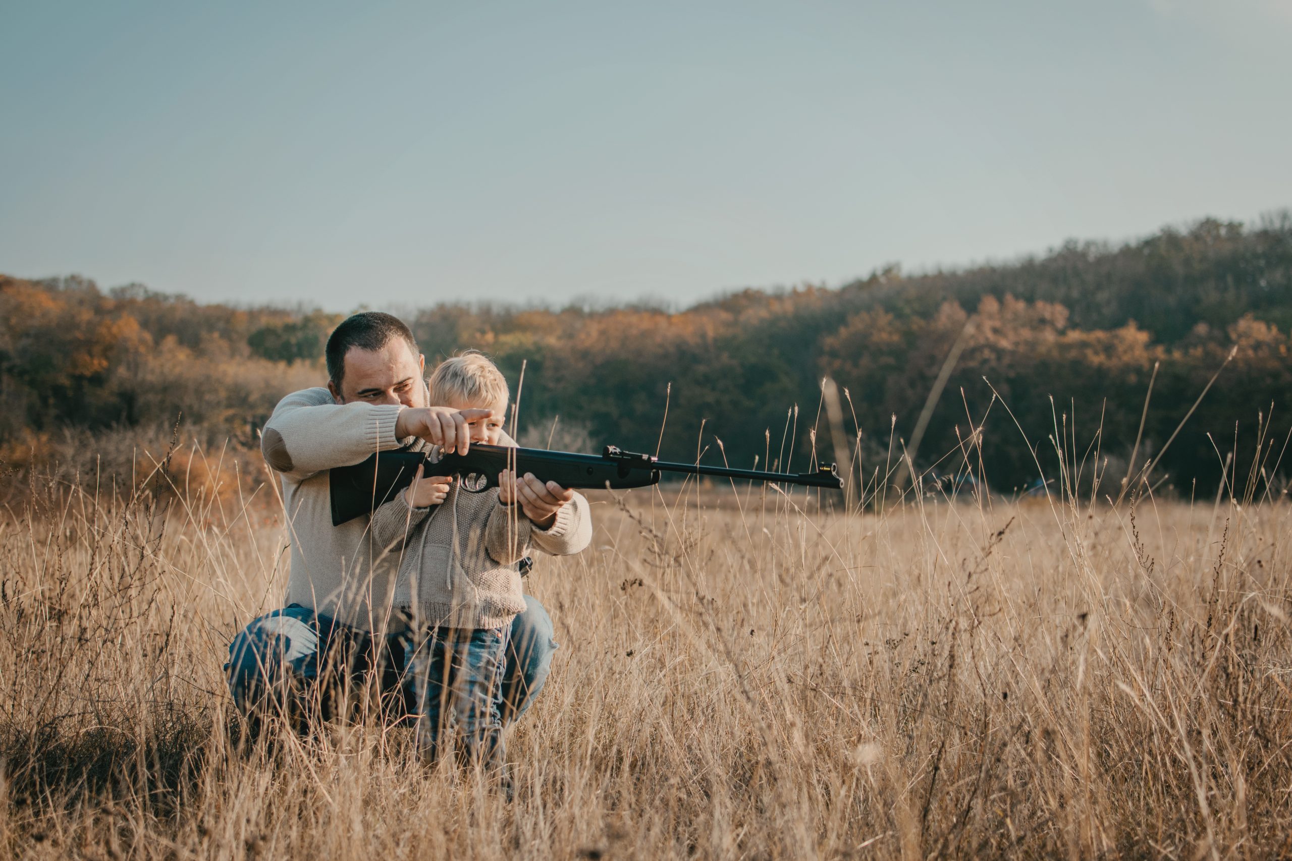 Father's day. Father with gun showing something to son while hunting on a nature. Happy family, Fathers Day and local summer vacation.