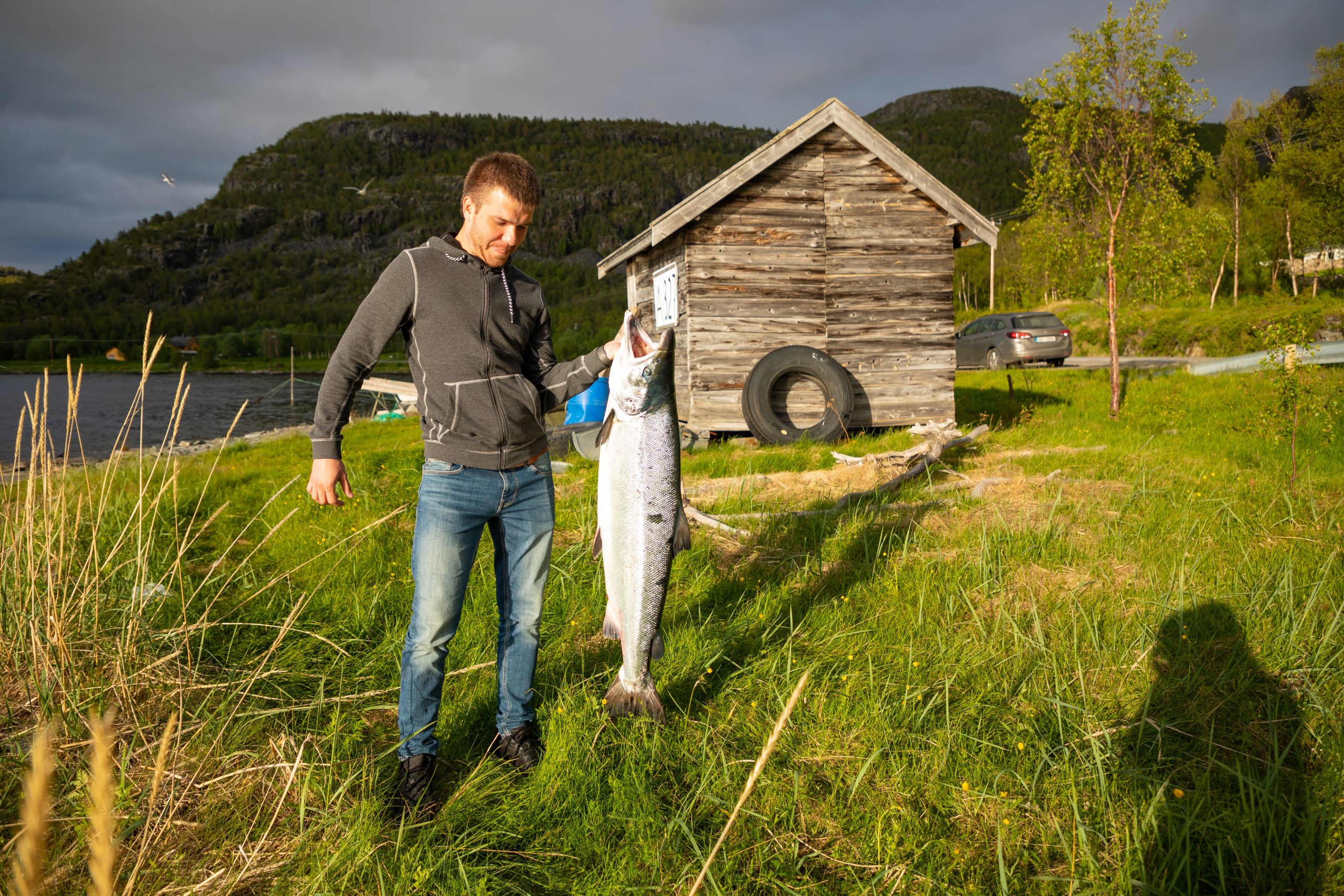man-holds-up-large-fish-on-grassy-shore-2026-03-20-02-10-12-utc