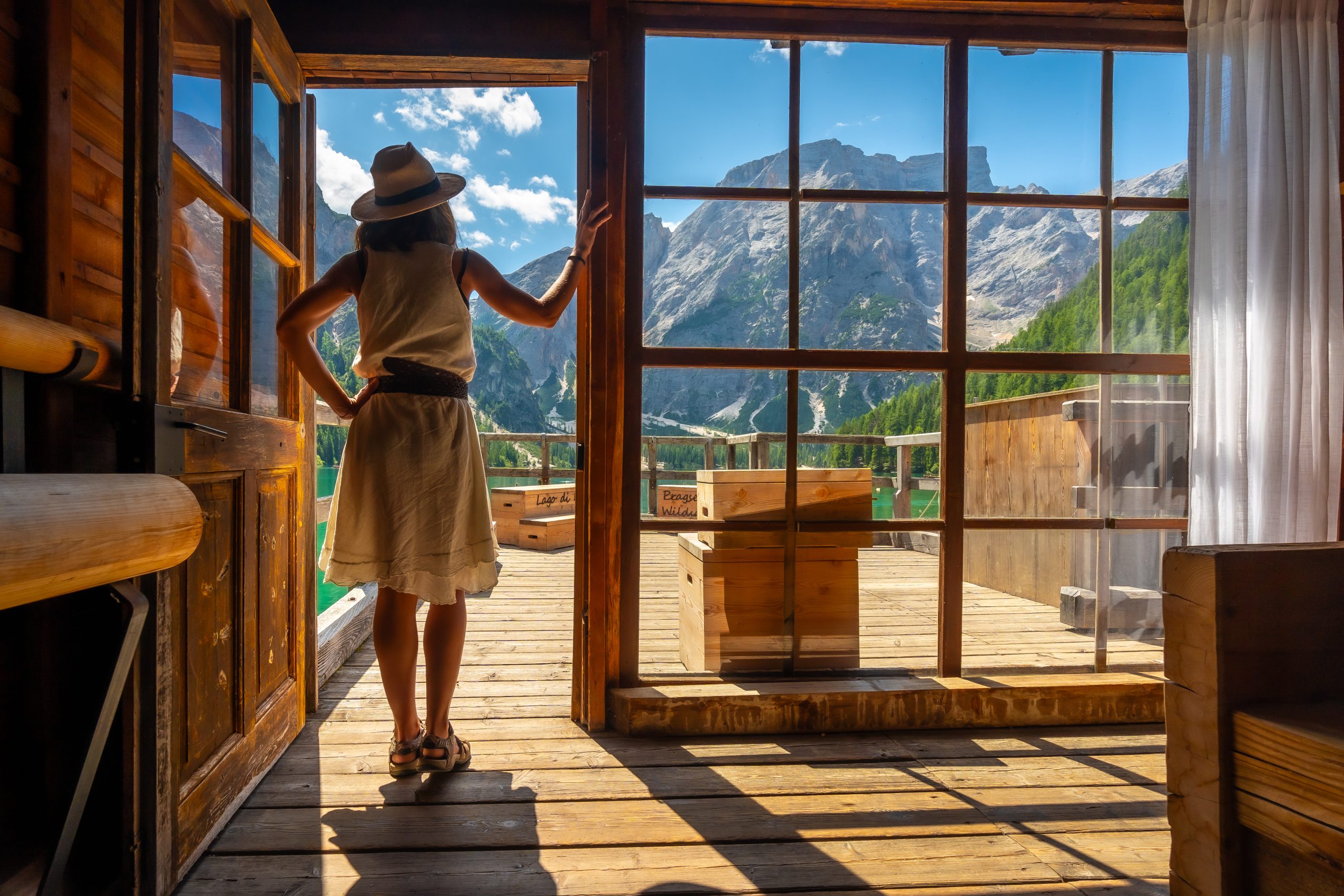 Woman enjoying breathtaking views of lake braies and surrounding mountains from a traditional wooden cabin in the italian dolomites